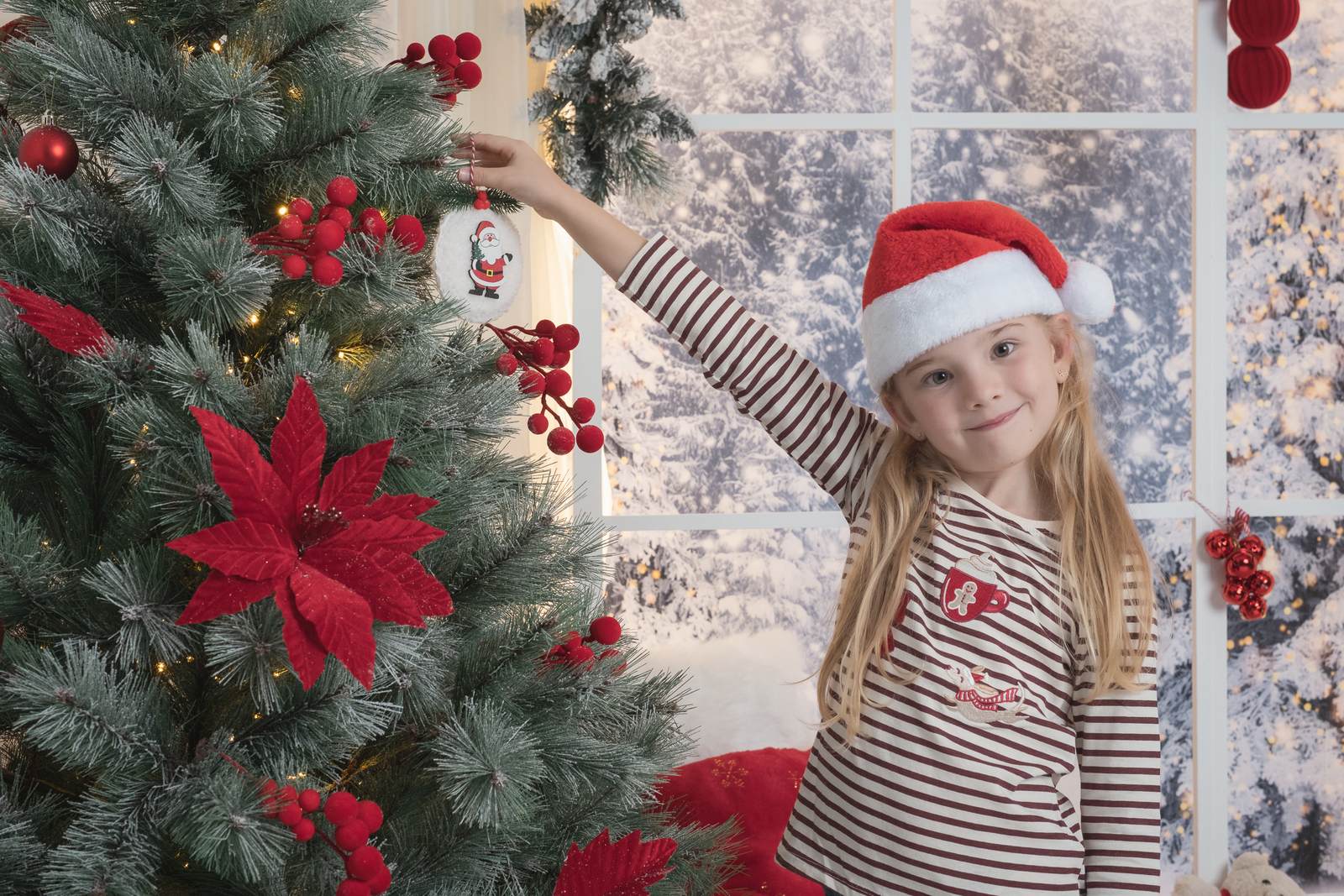 Niña con gorro de Papá Noel colgando un adorno en el árbol en una sesión de fotos de Navidad en Alicante
